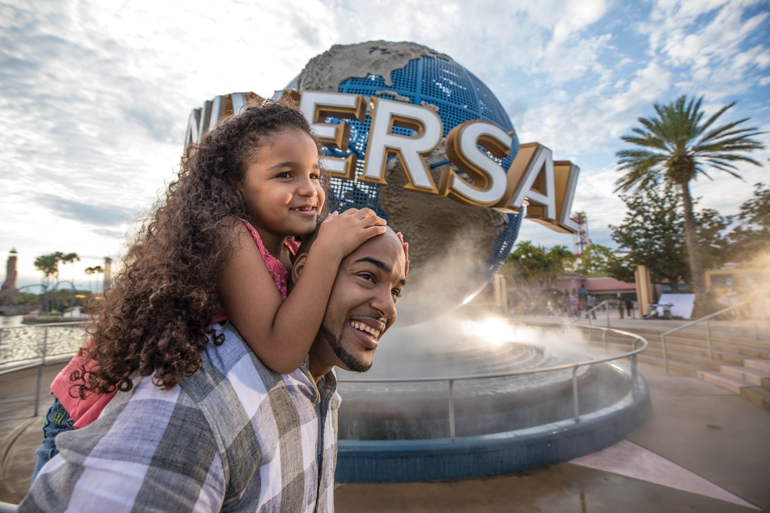 a father giving his daughter a piggyback ride in front of the Universal Studios globe statue