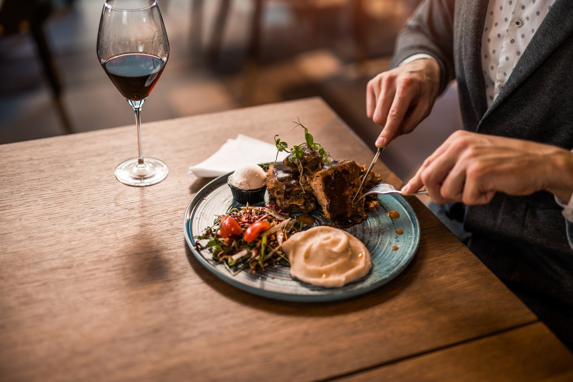 A man sitting at a wooden table cutting into a steak dinnr