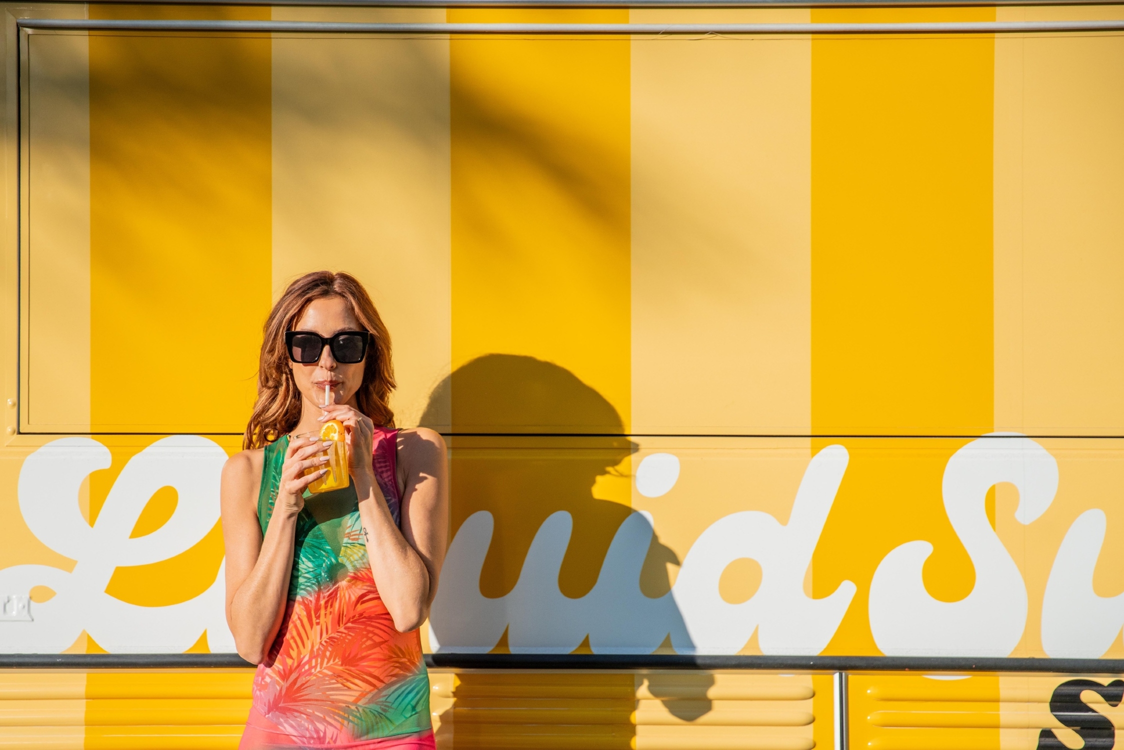 woman standing in front of a yellow food truck sipping a cocktail